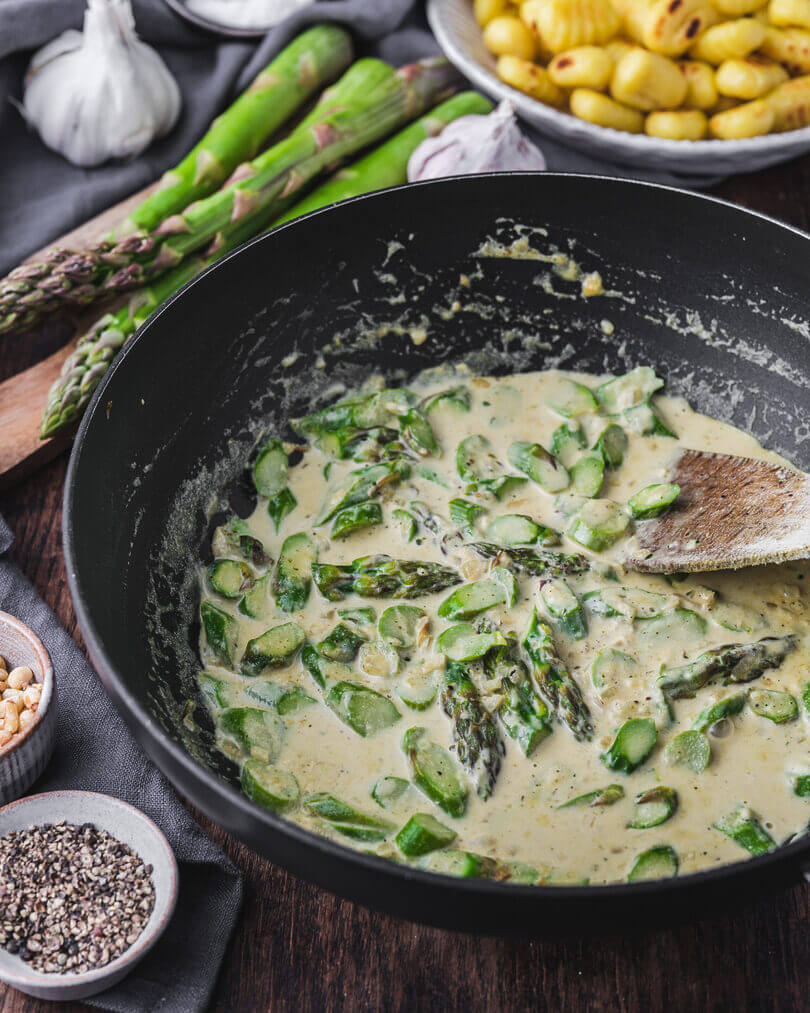 Grüner Spargel in cremiger Rahmsauce beim Kochen in der Pfanne für unsere vegetarische Gnocchi-Spargel-Pfanne.