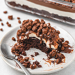 Servierstück des Krunchoco Cakes mit Schokoboden, Creme und Crunch-Topping auf einem Teller.