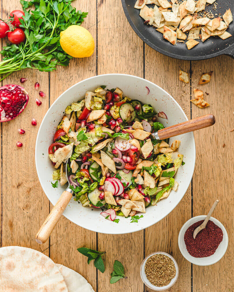 Fattoush-Salat von oben, angerichtet mit Tomaten, Gurke, Radieschen, Granatapfelkernen und geröstetem Fladenbrot