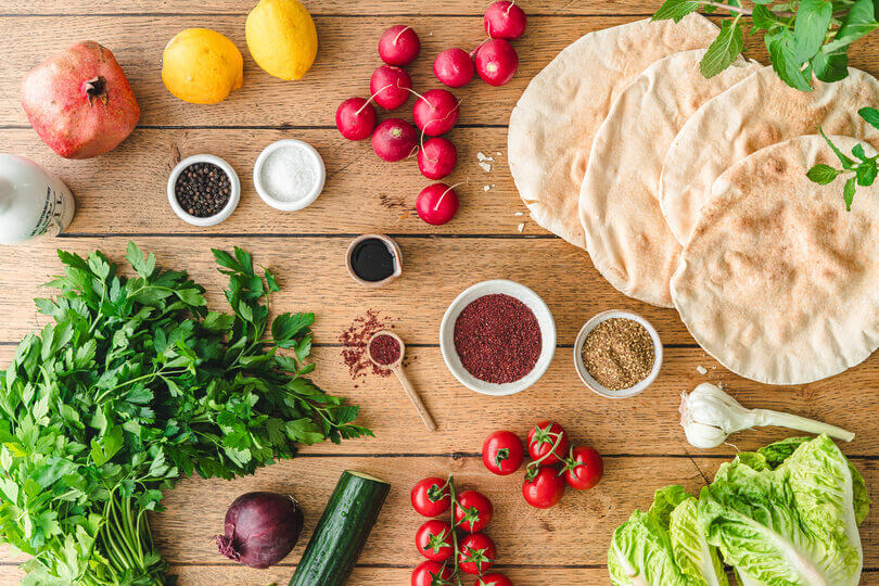 Zutaten für Fattoush: arabisches Fladenbrot, Tomaten, Gurke, Radieschen, Petersilie, Zwiebeln, Sumak, Za'atar, Granatapfelsirup etc. – typisch für libanesischen Brotsalat.