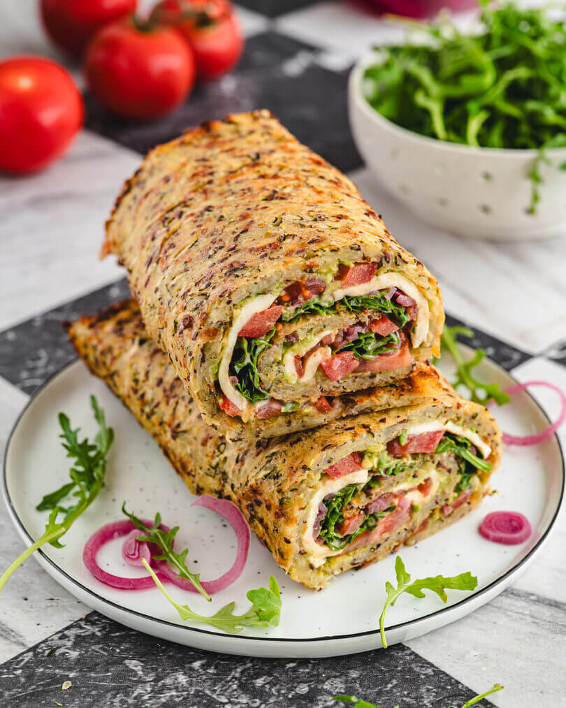 Aufgeschnittene Kartoffelrolle aus Gemüse mit Rucola, Tomaten und Käse – leckeres vegetarisches Gericht für Mealprep oder Mittagessen.