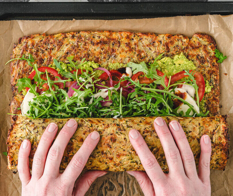 Zwei Hände rollen die mit Gemüse und Avocado belegte Gemüseroulade eng zusammen.