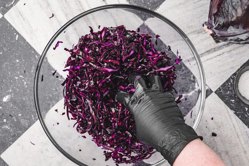 Person knetet geschnittenen Rotkohl mit schwarzen Handschuhen in einer Glasschüssel