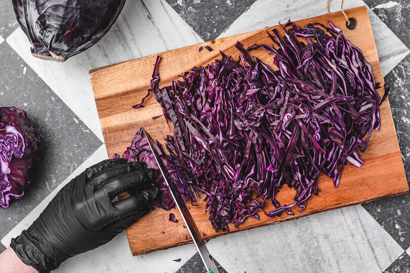 Frischer Rotkohl wird mit einem scharfen Messer auf einem Holzbrett in feine Streifen geschnitten